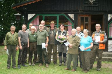 Gruppenfoto von Jägern vor einem Holzhaus, einige halten Urkunden und Blumen.
